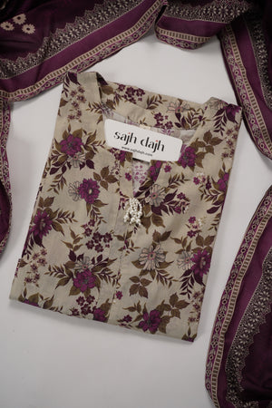 A folded beige kurta with a purple and brown floral print, featuring a silver-toned decorative collar and a white brand label reading 'sajh dach'. The kurta is styled with a matching purple and beige embroidered dupatta on a white background.